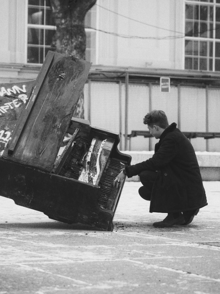 broken beautiful piano on ground with man playing black and white