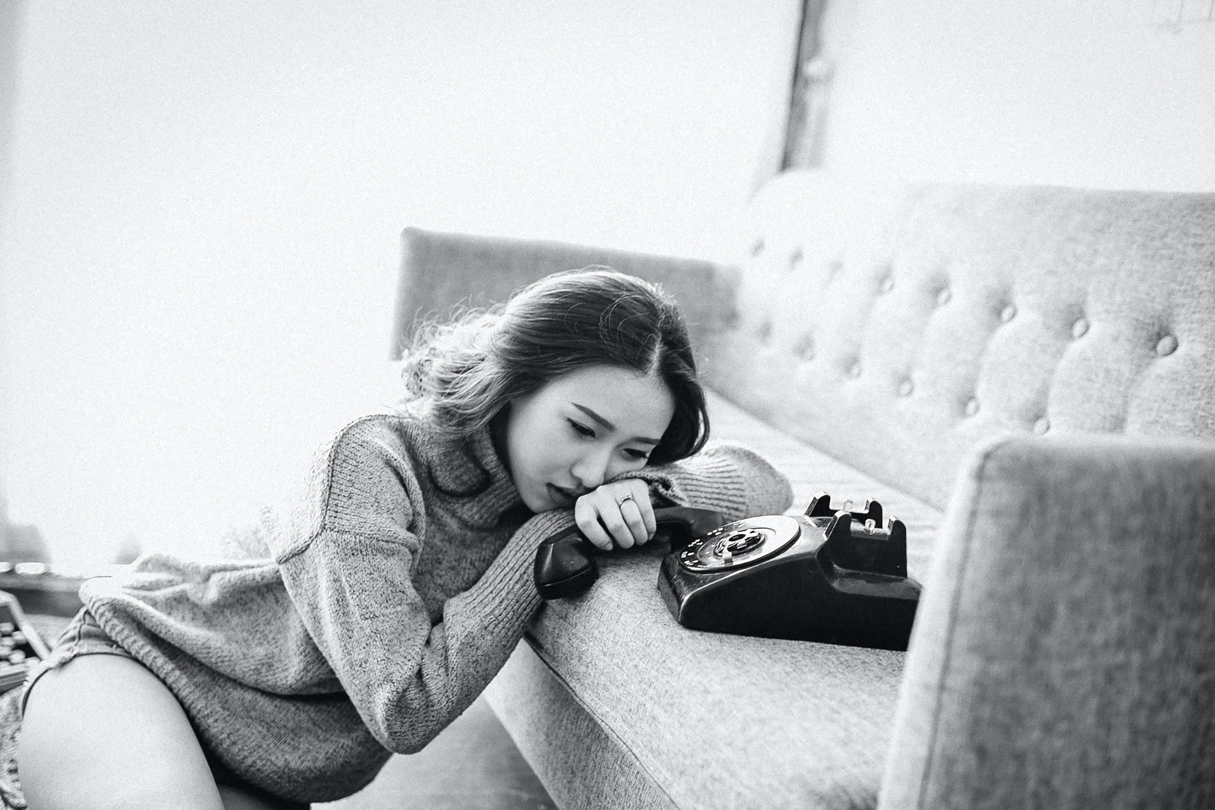 black and white picture of a woman holding the receiver to a phone with her head on the couch while sitting on the floor